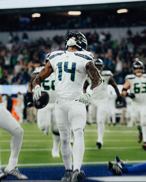 a football player running onto the field with his hands in his pockets and other players behind him