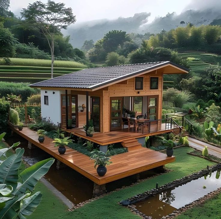 a small wooden house sitting on top of a lush green hillside next to a pond