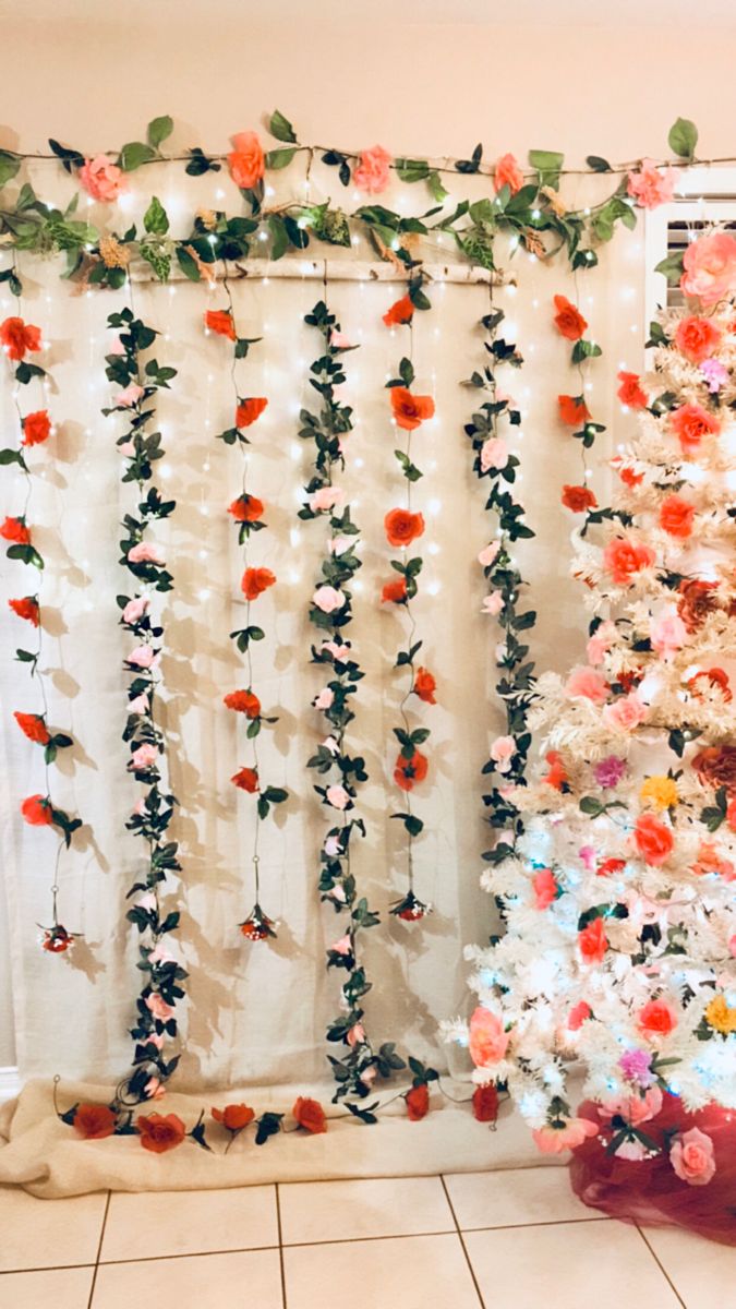 a decorated christmas tree in front of a white curtain with flowers on it and lights hanging from the side