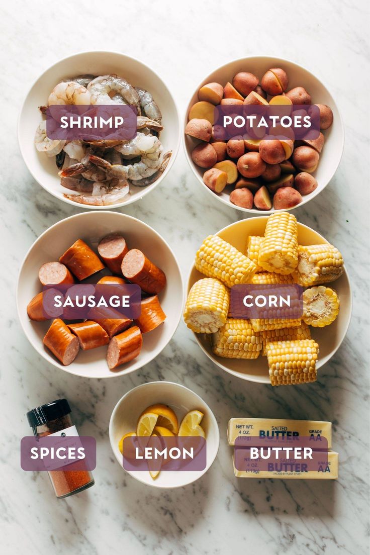 four bowls filled with different types of food on top of a marble countertop next to buttered potatoes, carrots, and corn