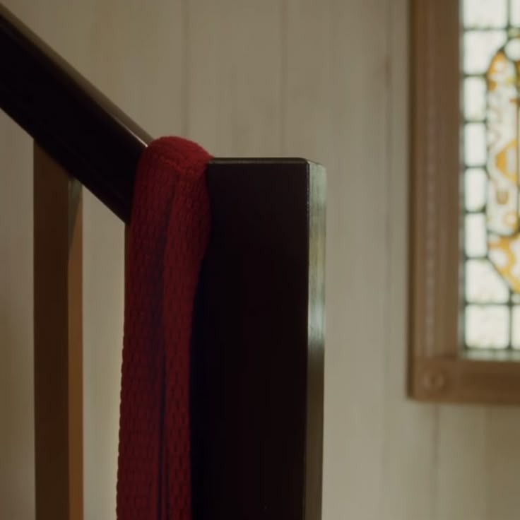 a red scarf hanging on the side of a wooden railing in front of a stained glass window