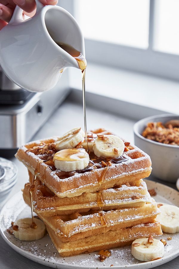 a stack of waffles with bananas and syrup being poured over them on a plate