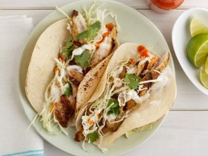 two tacos on a plate with limes and tomatoes