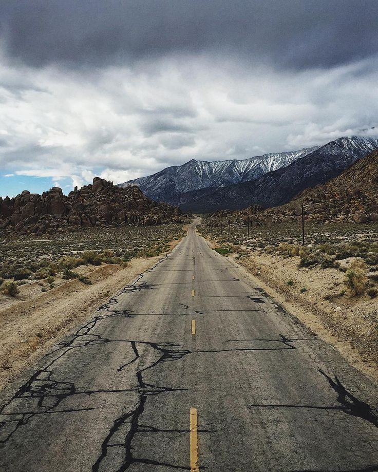 an empty road in the middle of nowhere with mountains in the background