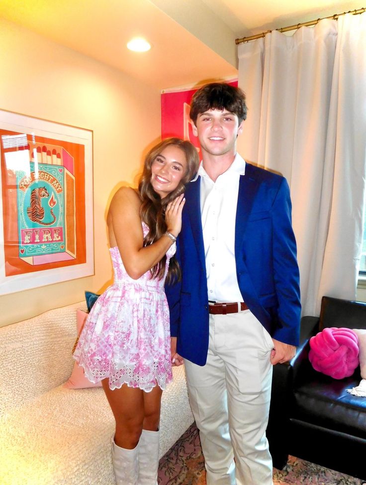 a young man and woman posing for a photo in their living room, with one holding the other's hand on her shoulder