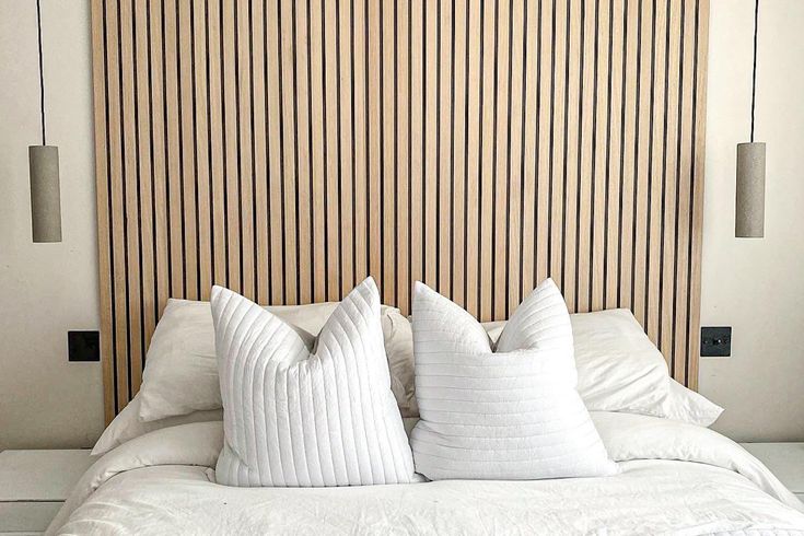 a white bed with two pillows on top of it next to a wooden headboard