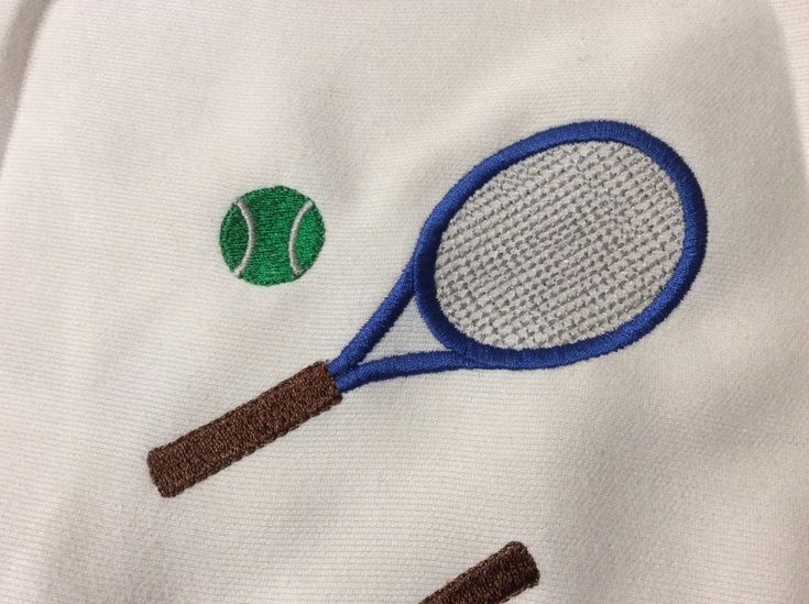 two tennis rackets and a ball embroidered onto a white t - shirt with blue trim