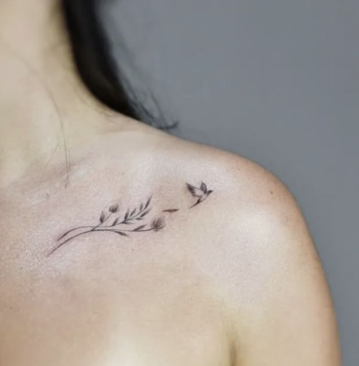 a woman's back shoulder with small tattoos on her left shoulder and flowers in the middle