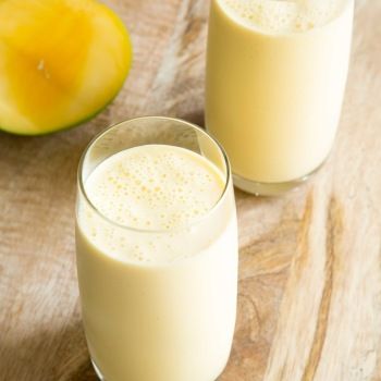 two glasses filled with milk next to an apple