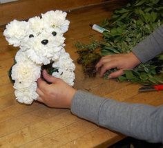 a person holding a stuffed animal in front of flowers on a wooden table with scissors