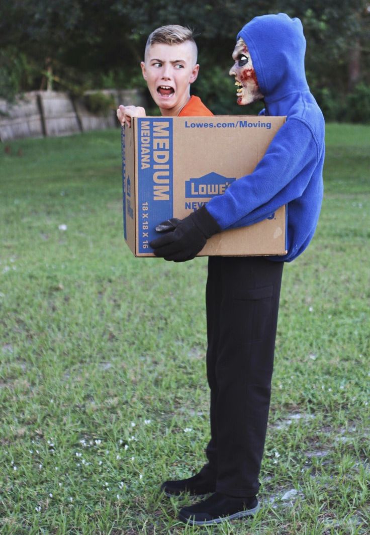 a man in a blue hoodie holding a cardboard box with an evil clown on it