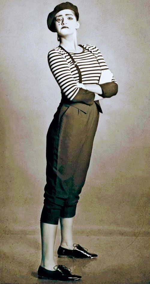 an old fashion photo of a woman in striped shirt and skirt standing with her arms crossed