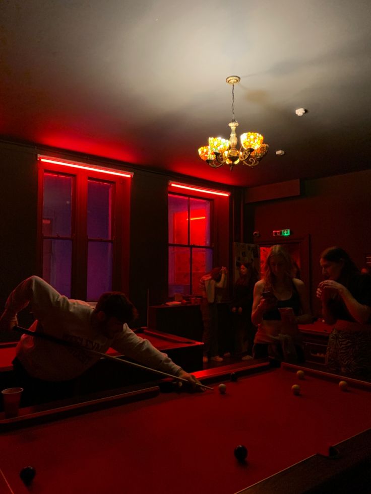 a man laying on top of a pool table in a room with red light coming from the ceiling