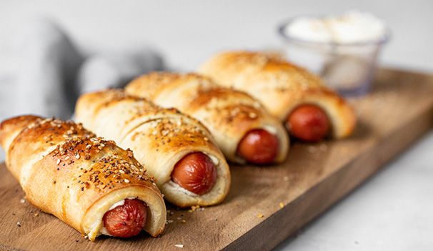 four hot dogs wrapped in bread on a cutting board