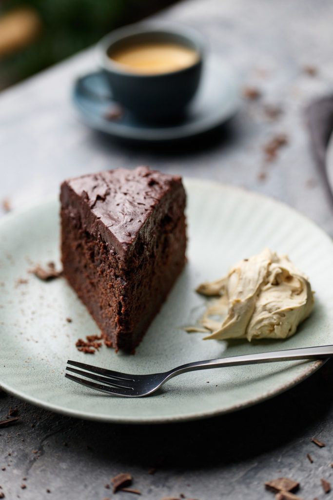 a piece of chocolate cake on a plate next to a fork and cup of coffee