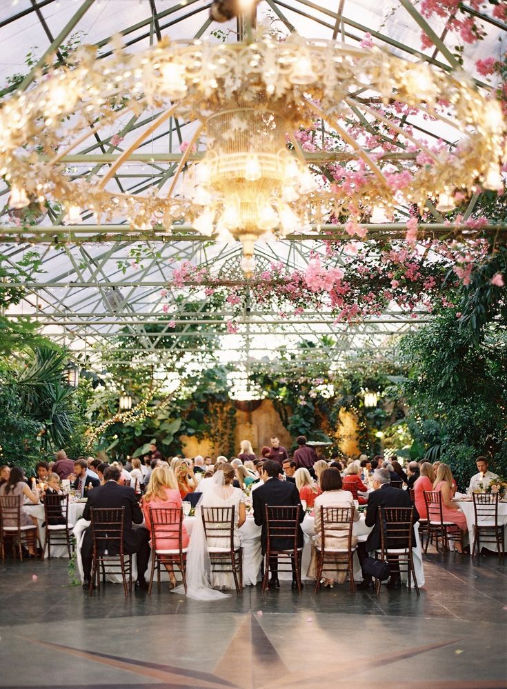 a large group of people sitting at tables in a room filled with plants and flowers