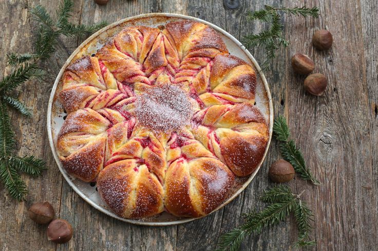 a pastry on a plate covered in powdered sugar and sliced almonds next to pine branches