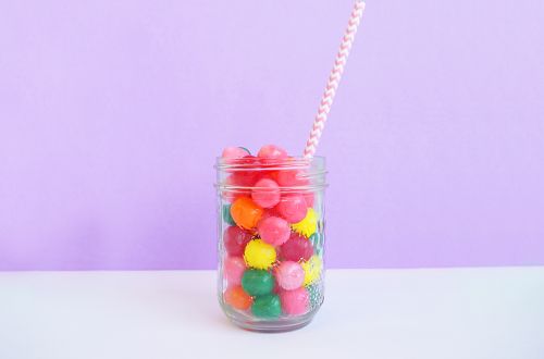 a jar filled with lots of colorful gummy balls next to a striped straw cup