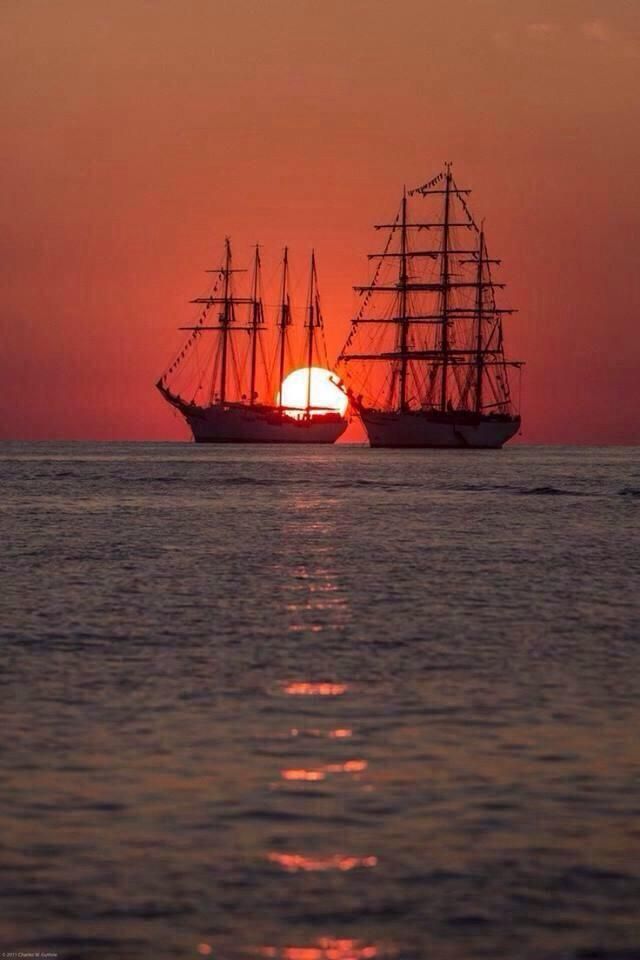 two ships are sailing in the ocean at sunset