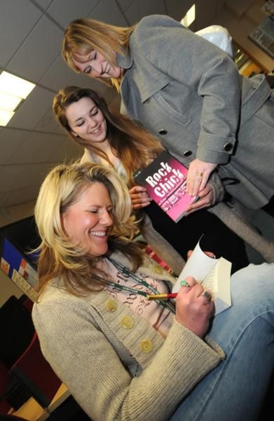 three women are smiling and posing for the camera while one woman is holding a book