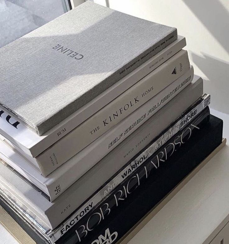 a stack of books sitting on top of a white table next to a glass window