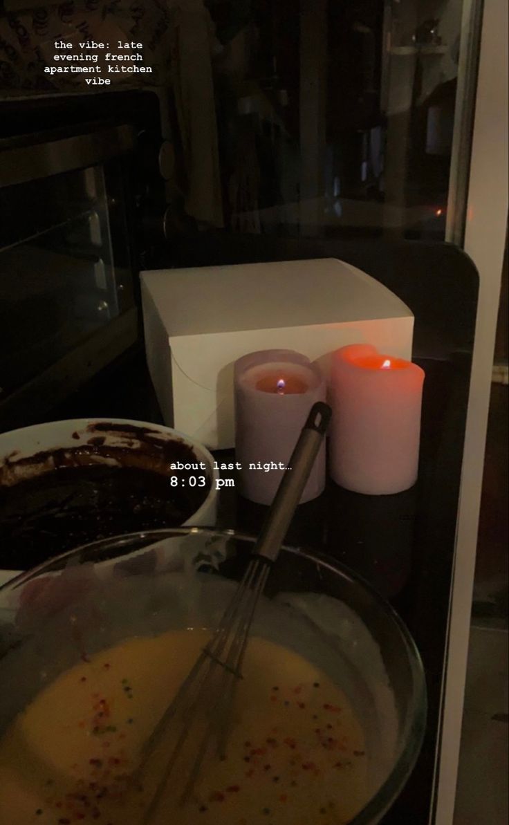 a glass bowl filled with food next to two candles and a box on the counter