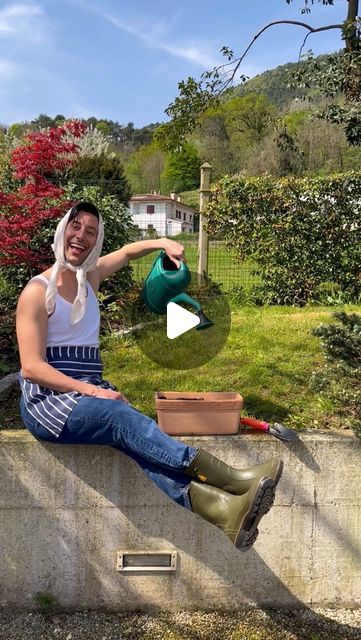 a man sitting on top of a cement wall holding a green watering can and potted plant