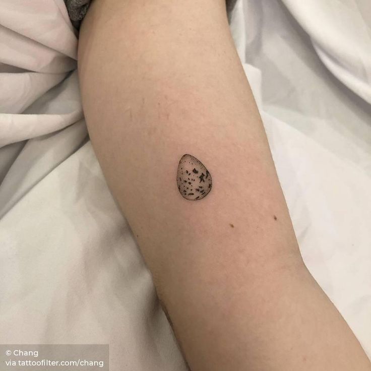 a small tattoo on the arm of a person laying in bed with a white sheet