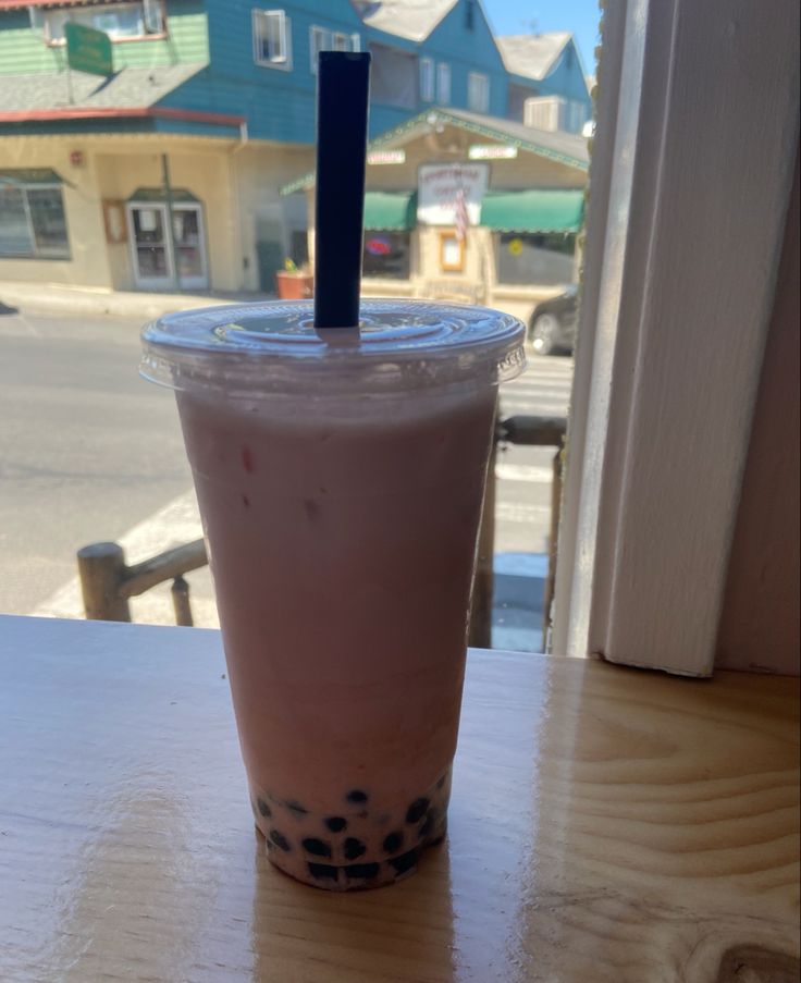 a drink sitting on top of a wooden table next to a window with a blue stick sticking out of it