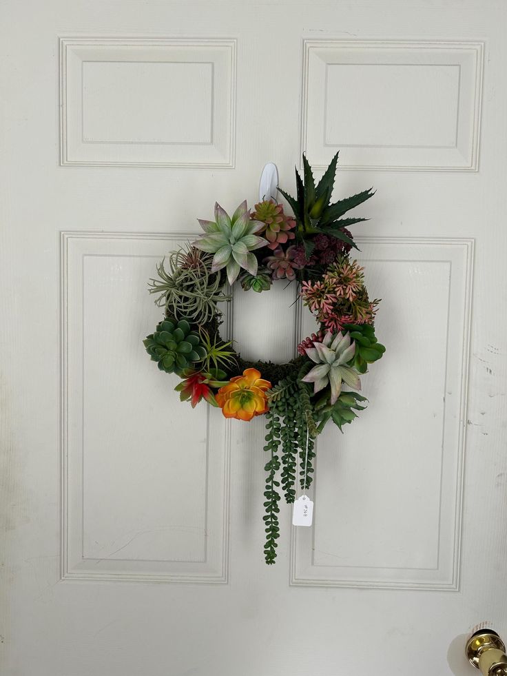 a wreath hanging on the front door with succulents and candles