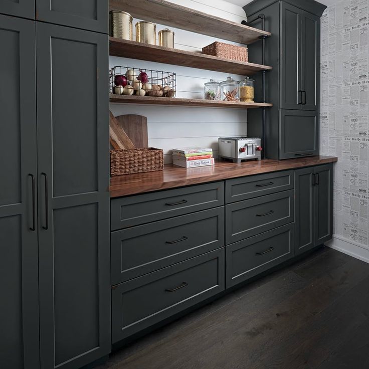 a kitchen with gray cabinets and wooden counter tops, along with baskets on the shelves