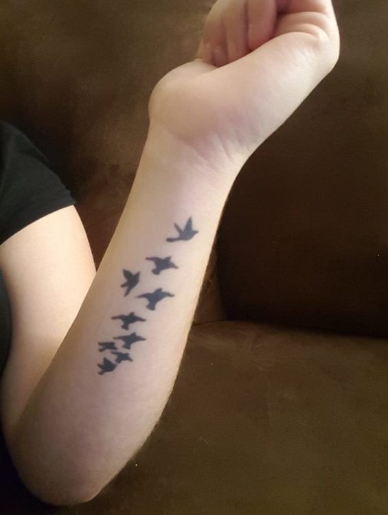 a woman with a tattoo on her arm that has birds flying in the sky above her arm