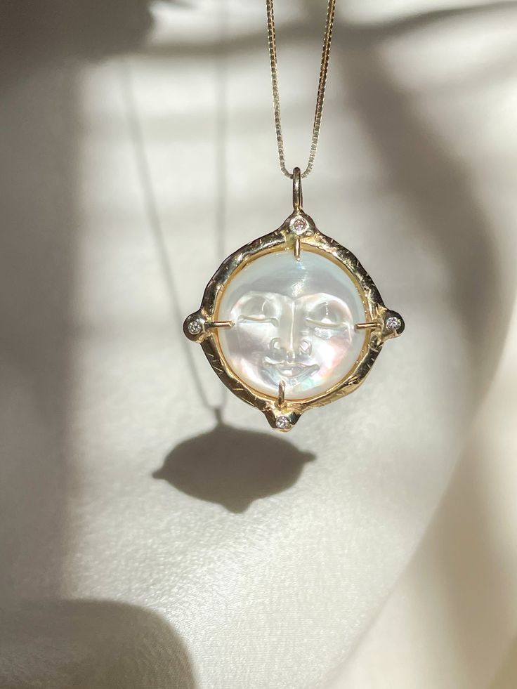 A dreamy 15mm hand-carved Mother of Pearl Moon encircled in gold, set with (4) White Diamonds, set on a solid 14k yellow gold 0.8mm box chain. (Approx. 5.7g.) Inspired in essence by the Impressionist French composer Claude Debussy, Clair de Lune translates to pale blue light or moonlight, and embodies the Divine Feminine energy of the moon, wholly encapsulating the deep sense of serenity found through inner self-awareness, and the strength kept within the gentleness of the heart. Aligns with int White Sun And Moon Round Pendant Jewelry, White Sun And Moon Design Round Pendant Jewelry, White Celestial Jewelry, Celestial Jewelry With Coin Pendant For Anniversary, White Sun And Moon Pendant Jewelry, White Pendant Jewelry With Sun And Moon Design, White Round Celestial Jewelry, White Sun And Moon Design Pendant Jewelry, Celestial Medallion Jewelry For Anniversary