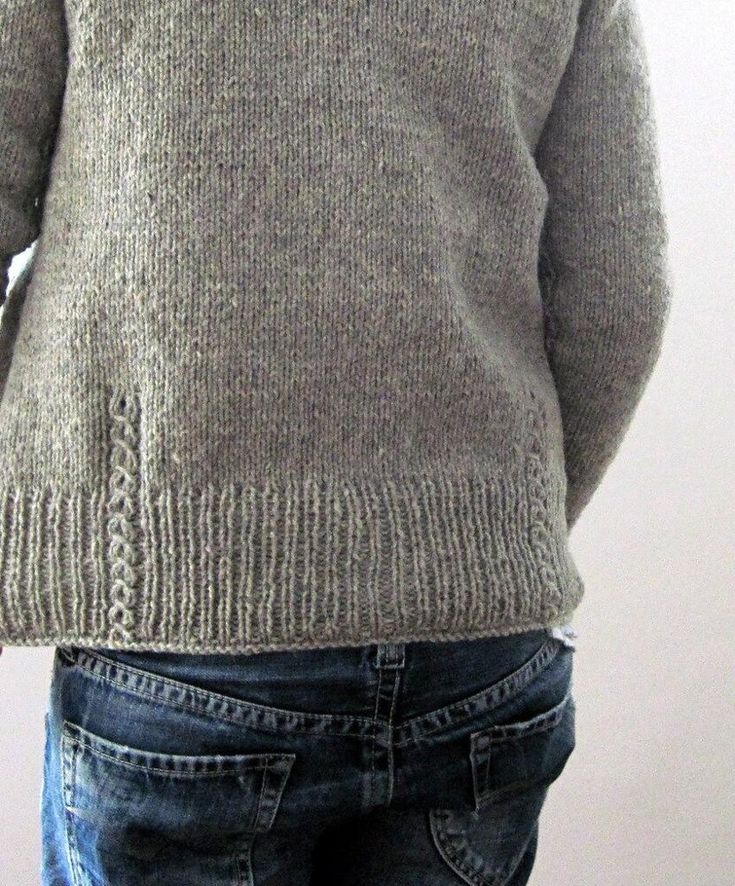 the back of a man's sweater with his hands in his pockets, standing against a white wall