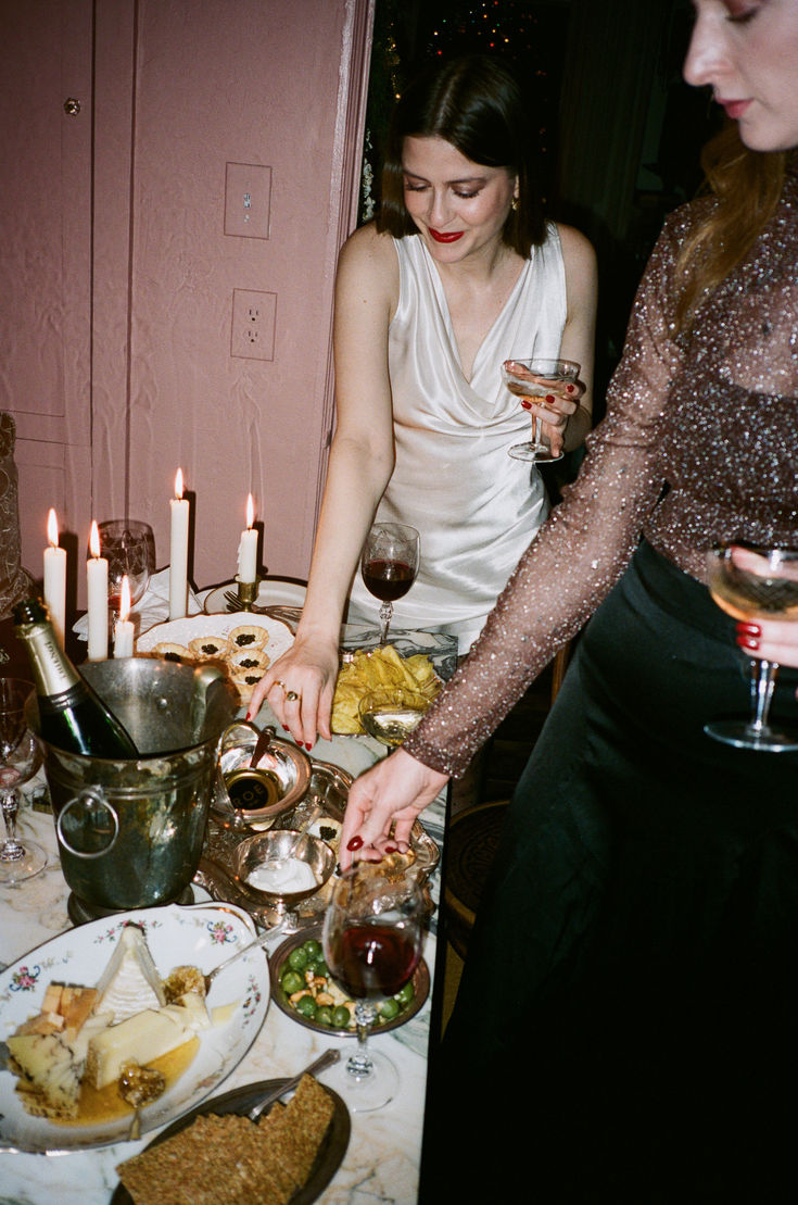 two women standing at a table with food and wine