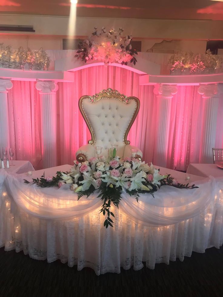 a fancy chair with flowers and greenery on the table in front of pink drapes