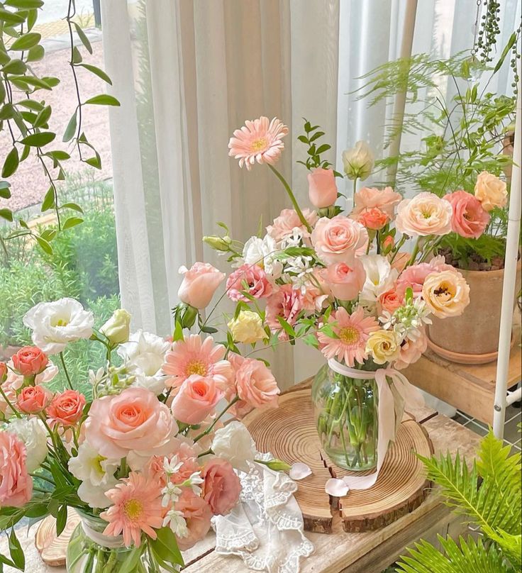 a vase filled with pink and white flowers on top of a table next to potted plants