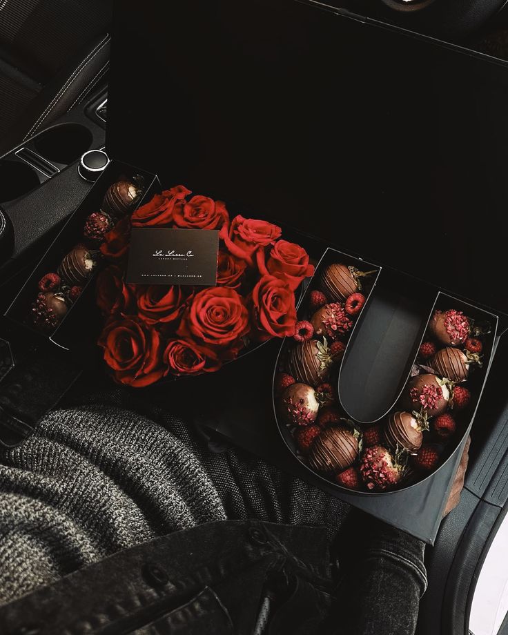 roses and chocolates in a black box on the floor next to a person's feet