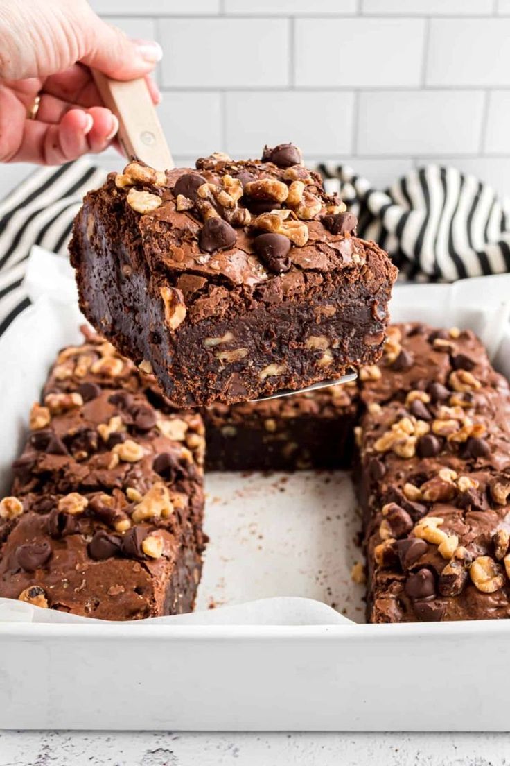 a person holding a spoon over some brownies in a white dish with chocolate chips on top