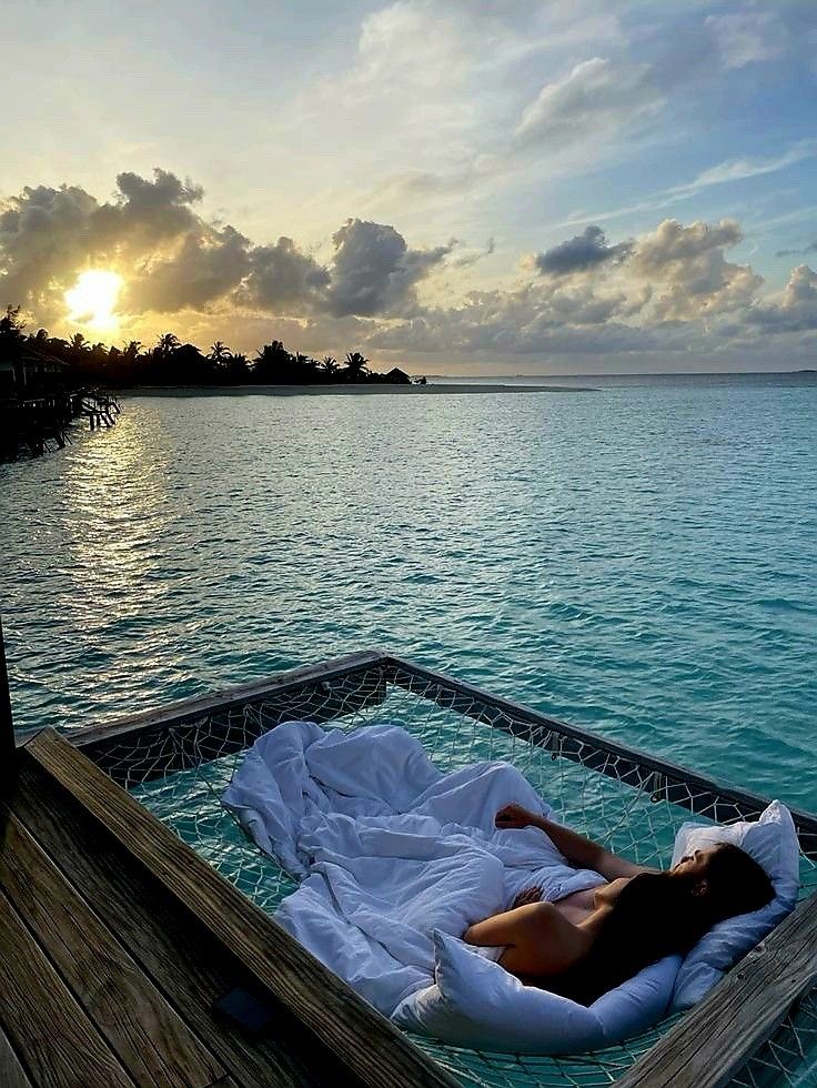 a woman laying in a hammock on top of the water at sunset or dawn