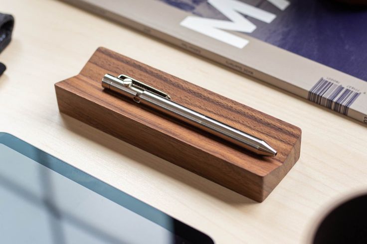 a wooden pen holder with a metal ballpoint pen on it sitting on a desk