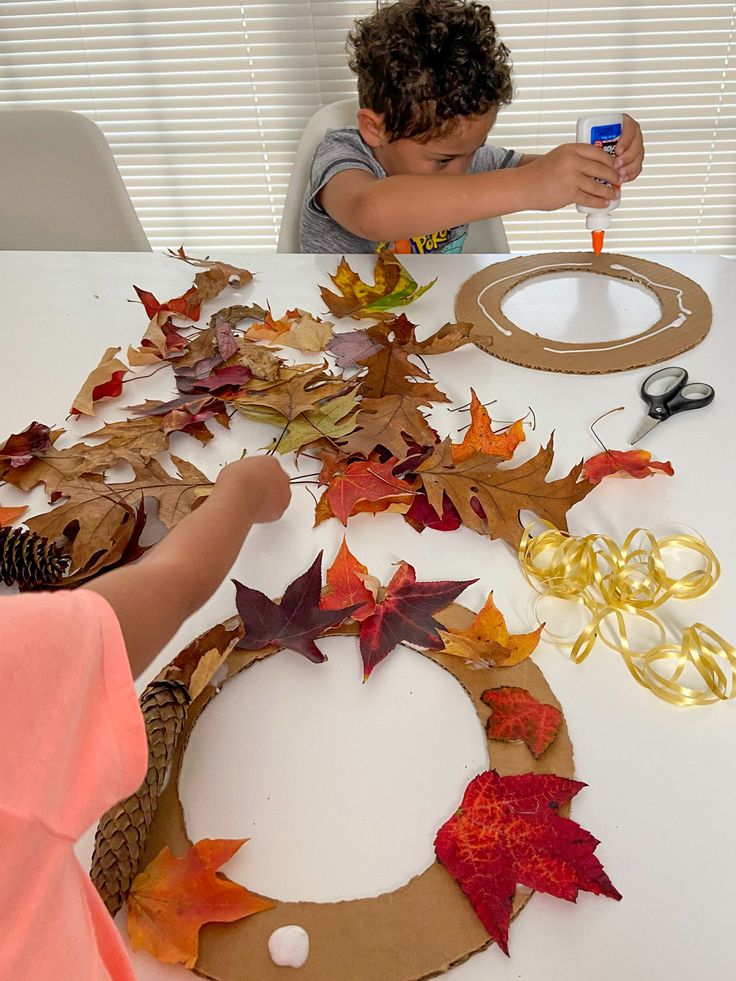 two children are making fall leaves out of construction paper on a table with scissors and tape