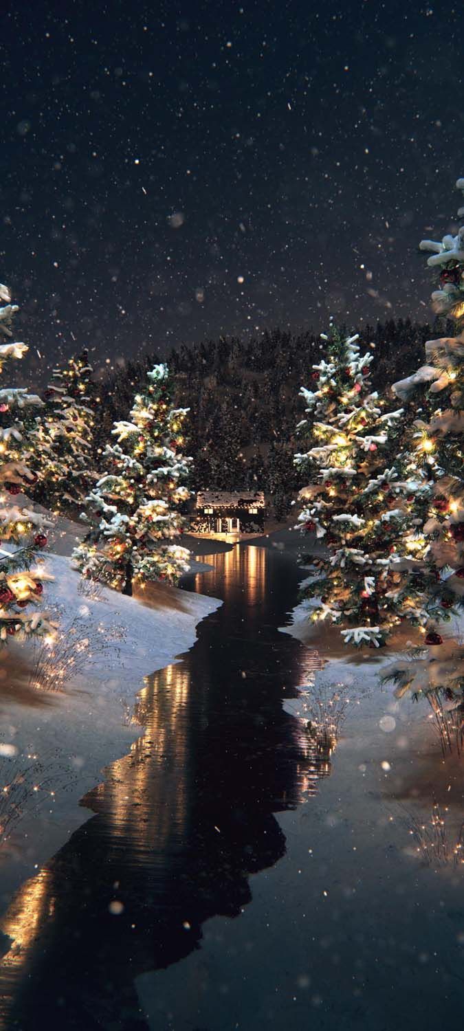 christmas trees are lit up and reflecting in the water at night with snow falling on them