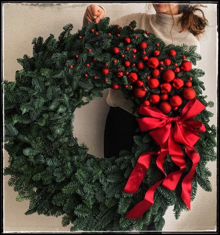 a woman holding a christmas wreath with red balls and bows on it's front