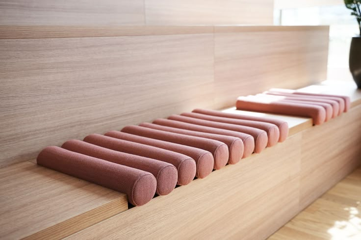 a row of pink cushions sitting on top of a wooden shelf next to a potted plant