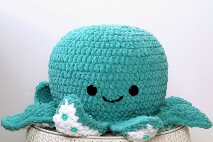 a crocheted blue octopus stuffed animal sitting on top of a white basket with flowers