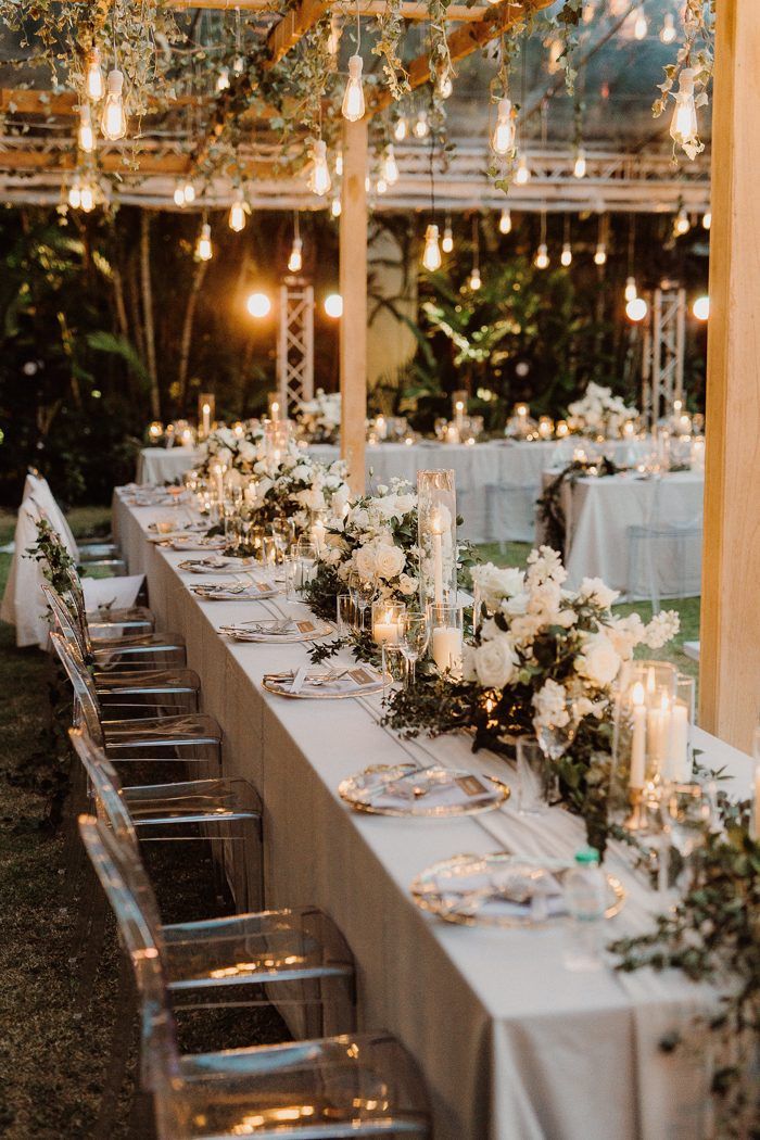 a long table with white flowers and candles on it is set for an outdoor dinner