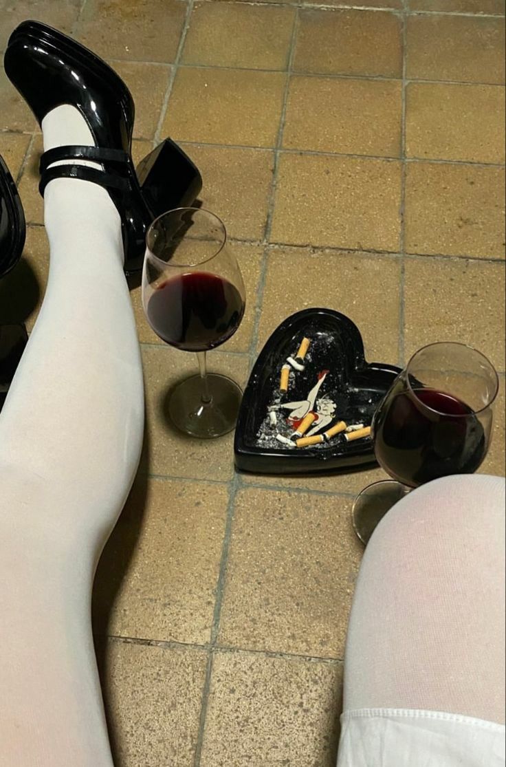 a woman's legs and feet with wine glasses on the floor next to her