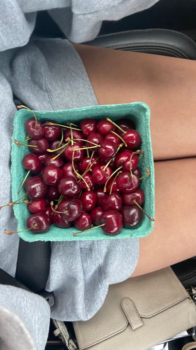 a woman's legs holding a green bowl filled with cherries