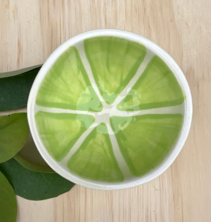 a green and white bowl sitting on top of a wooden table next to a plant